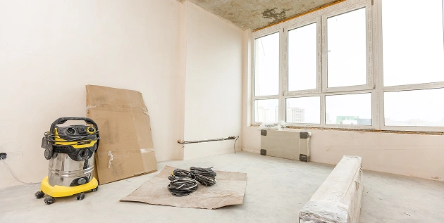 Een lege, lichte kamer met grijze muren, licht laminaat en een raam.