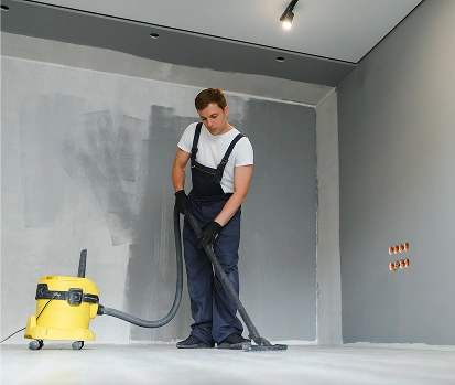 Een man in een blauwe bouwpakket ruimt de ruimte op met behulp van een bouwstofzuiger, ter voorbereiding op de volgende fase van de renovatie.