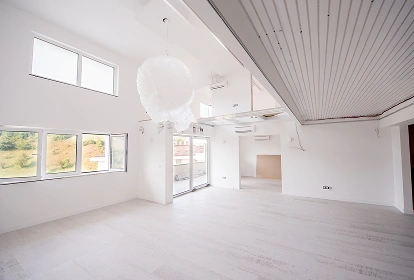 Lichte woonkamer in een huis met twee verdiepingen en grote ramen, momenteel in renovatie.