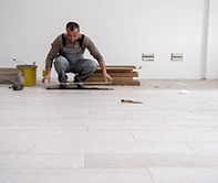 Een man in een bouwpakket legt parket in een lichte kamer.